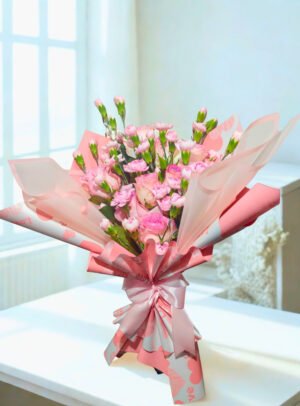 Ramo floral elegante en tonos rosados con rosas y mini claveles, envuelto en papel coreano translúcido y lazo satinado rosa.