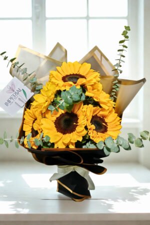 Ramo elegante de girasoles amarillos premium con eucalipto natural y envoltorio negro con detalles dorados.