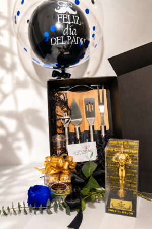 Caja regalo para el Día del Padre con set parrillero, globo personalizado, rosa azul, chocolates y trofeo decorativo en presentación elegante negra.