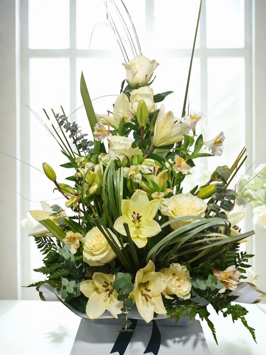 Centro floral elegante con lirios orientales blancos, rosas blancas premium, alstroemerias y follajes verdes en diseño vertical sofisticado.