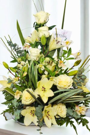 Centro floral elegante con lirios orientales blancos, rosas blancas premium, alstroemerias y follajes verdes en diseño vertical sofisticado.