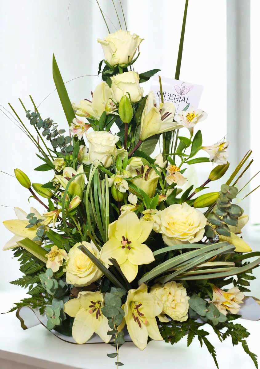 Centro floral elegante con lirios orientales blancos, rosas blancas premium, alstroemerias y follajes verdes en diseño vertical sofisticado.