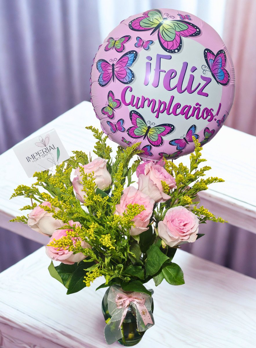 Arreglo floral de cumpleaños con rosas rosadas, solidago amarillo, florero de vidrio y globo decorativo de mariposas con mensaje Feliz Cumpleaños.