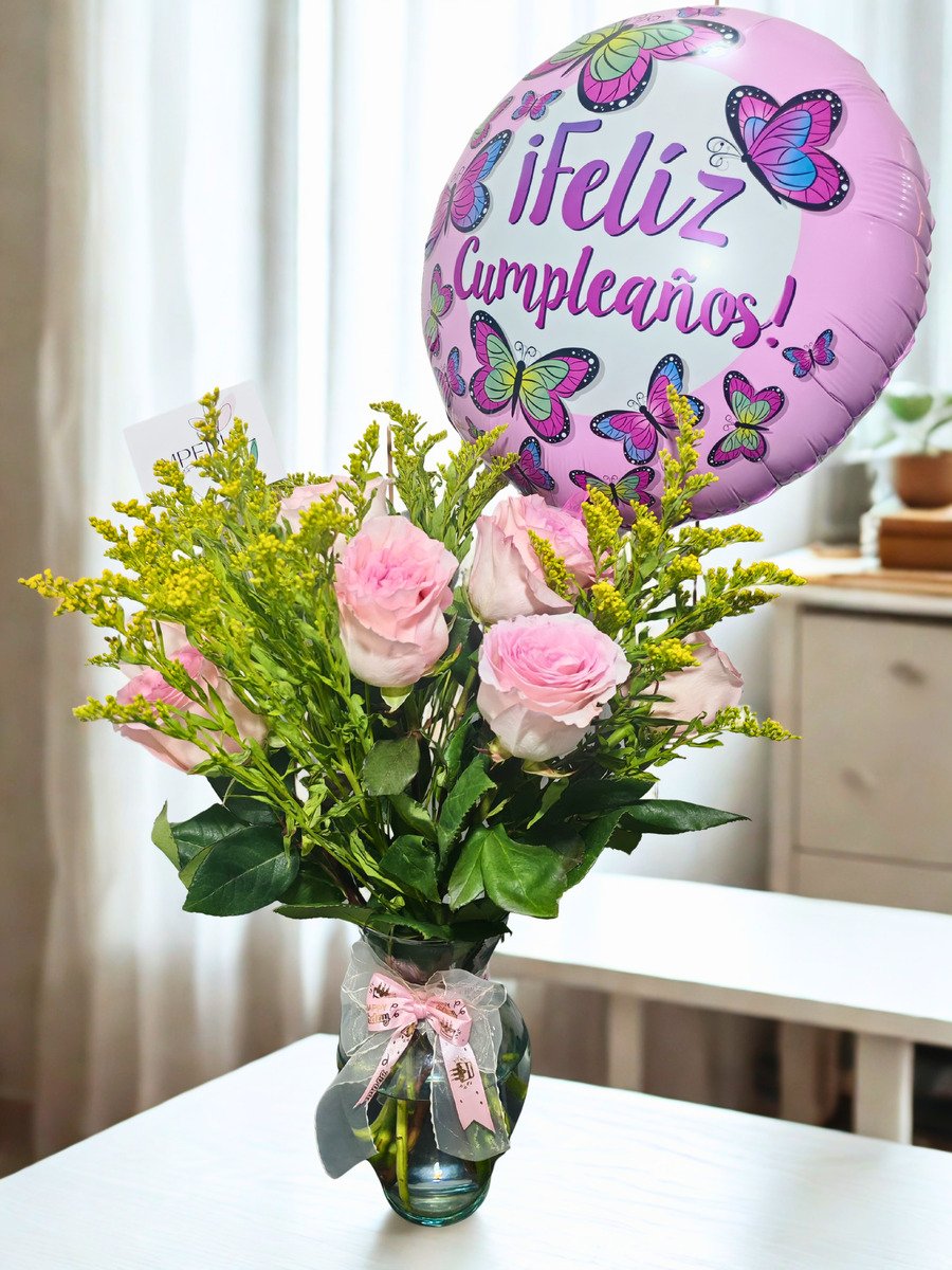 Arreglo floral de cumpleaños con rosas rosadas, solidago amarillo, florero de vidrio y globo decorativo de mariposas con mensaje Feliz Cumpleaños.