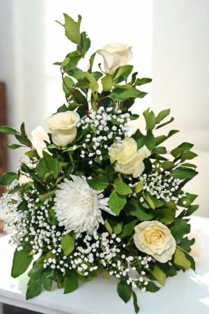 Arreglo floral de condolencias con cinco rosas blancas, gypsophila y follaje en balde metálico decorativo.