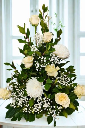 Pie de urna floral con cuatro rosas blancas, crisantemo Spider, gypsophila y follaje ornamental.