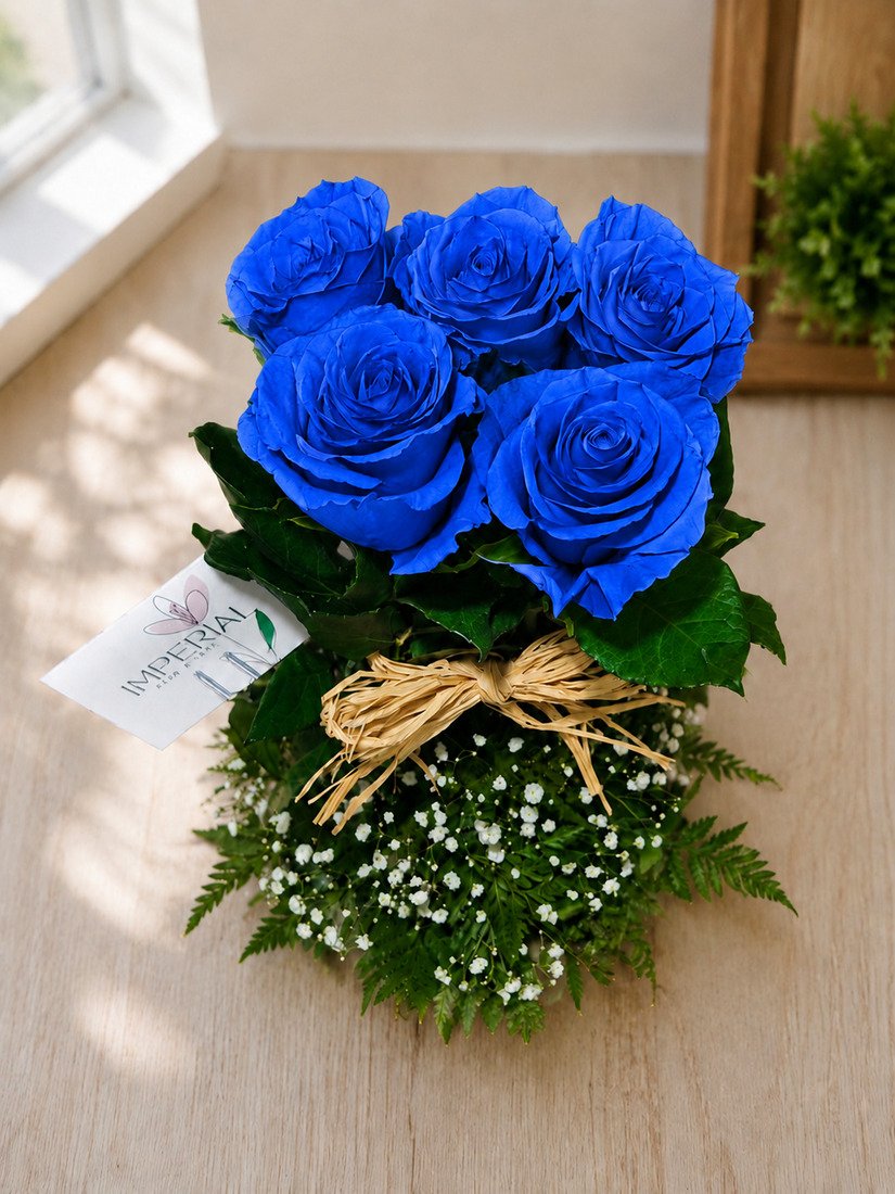 Arreglo floral de cinco rosas azules con gypsophila, follaje natural y lazo decorativo en base elegante.